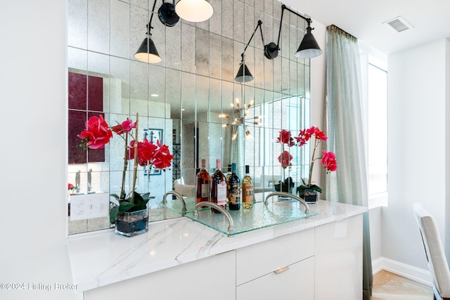 bar with decorative light fixtures, white cabinetry, and light stone counters