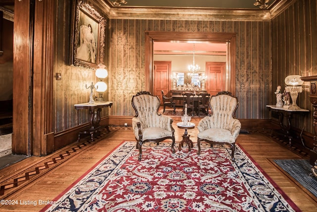 living area with a chandelier, wood-type flooring, wooden walls, and crown molding