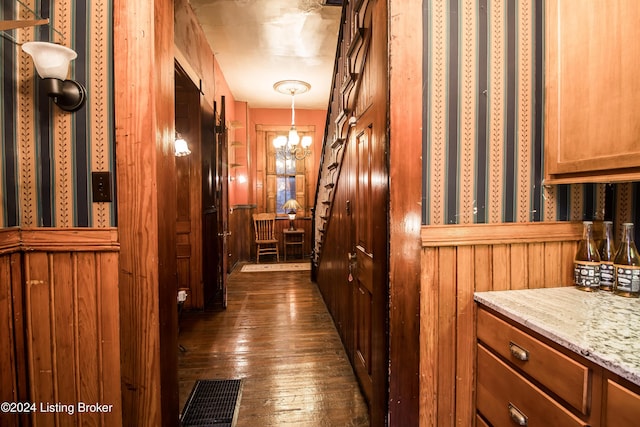 corridor with dark hardwood / wood-style floors, an inviting chandelier, and wooden walls