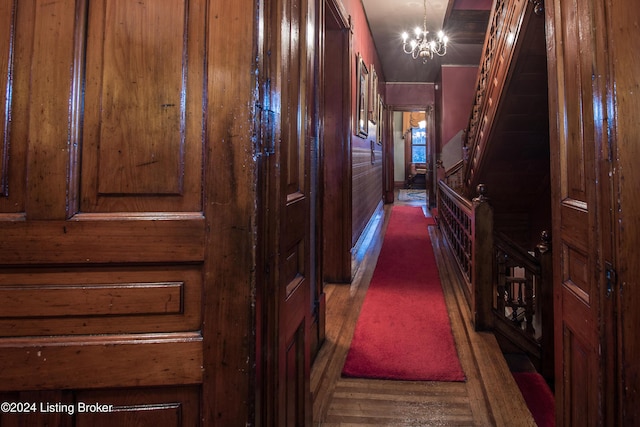 hall with wooden walls, dark hardwood / wood-style flooring, and a chandelier