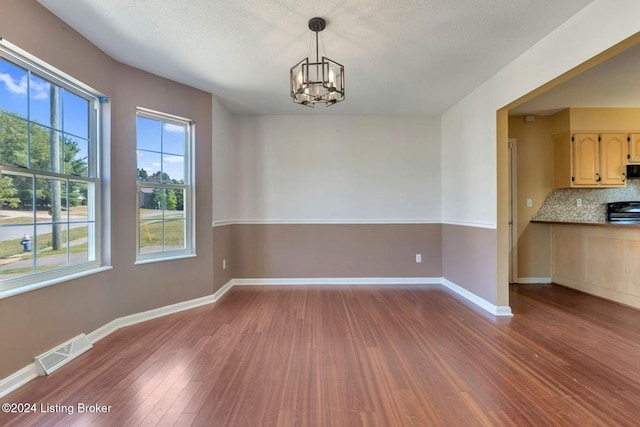 unfurnished dining area featuring hardwood / wood-style floors, a textured ceiling, and a notable chandelier