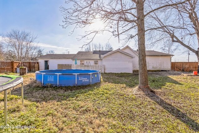 rear view of house with a lawn, a fenced in pool, and a trampoline