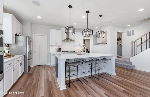 kitchen with white cabinets, light hardwood / wood-style floors, a kitchen island with sink, and hanging light fixtures