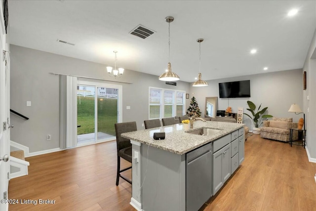 kitchen featuring dishwasher, sink, gray cabinets, an island with sink, and a kitchen bar