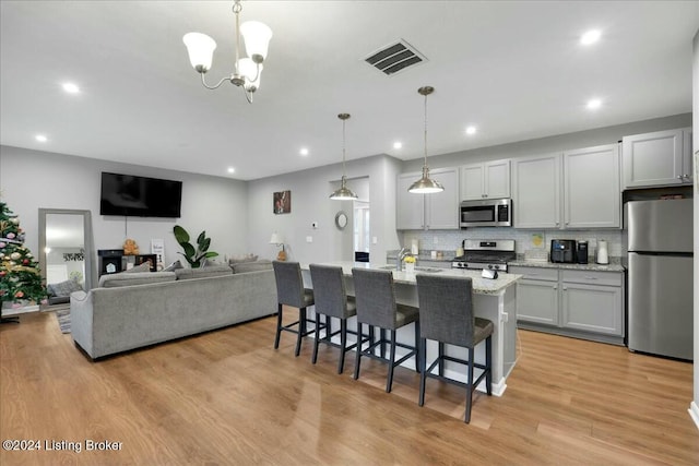 kitchen featuring light stone countertops, hanging light fixtures, stainless steel appliances, a breakfast bar area, and a kitchen island with sink