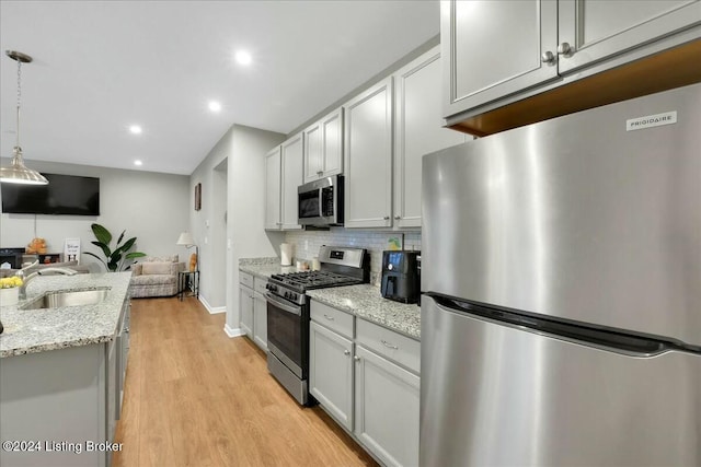 kitchen featuring sink, light wood-type flooring, decorative light fixtures, light stone counters, and stainless steel appliances