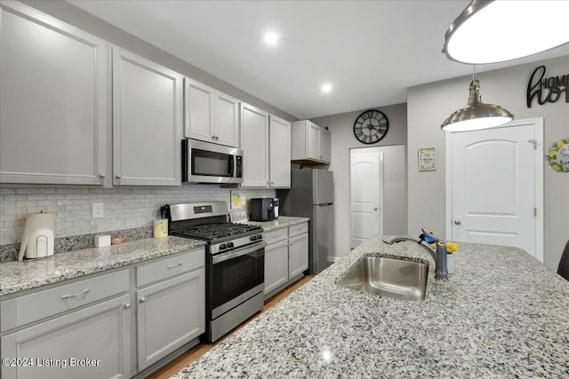 kitchen featuring sink, light stone counters, pendant lighting, decorative backsplash, and appliances with stainless steel finishes