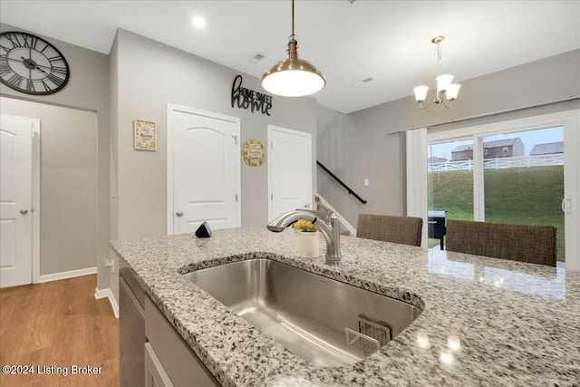 kitchen featuring hardwood / wood-style floors, a notable chandelier, sink, light stone countertops, and decorative light fixtures