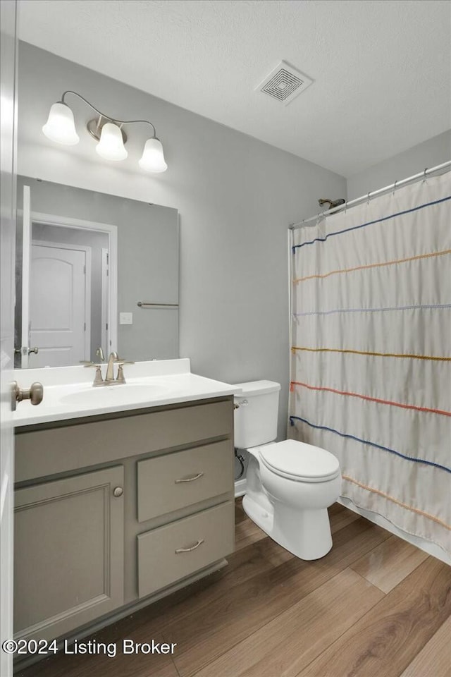 bathroom featuring a shower with curtain, vanity, a textured ceiling, hardwood / wood-style flooring, and toilet