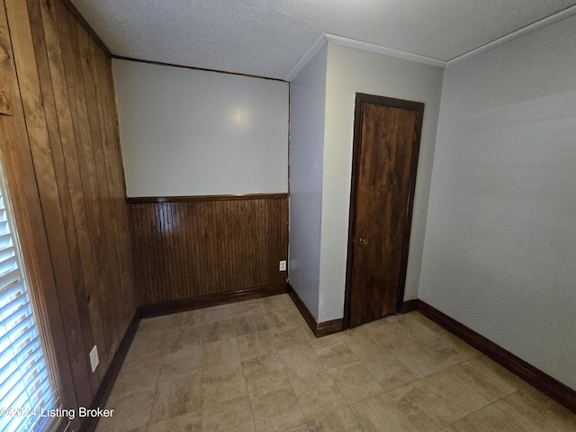 spare room featuring wood walls, crown molding, and a textured ceiling