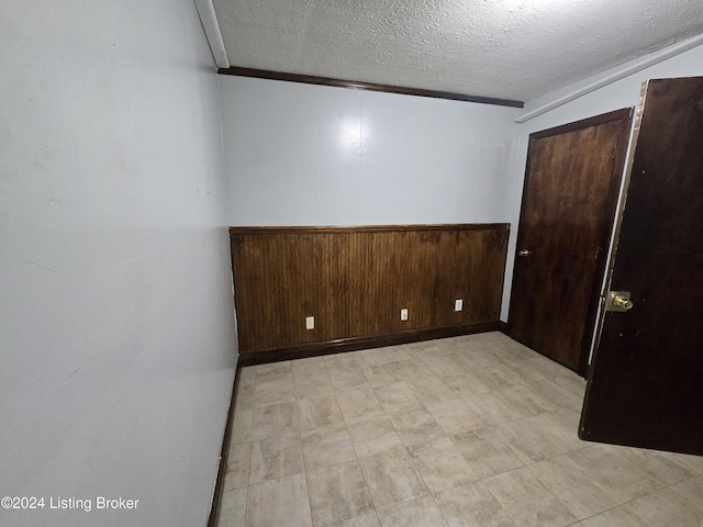 unfurnished room featuring ornamental molding, a textured ceiling, and wooden walls