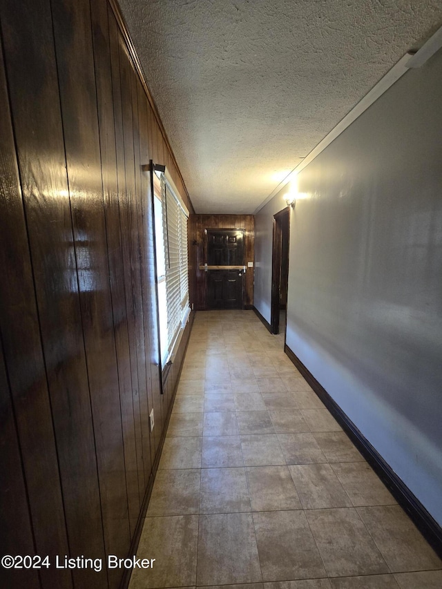 hallway featuring a textured ceiling, wood walls, and crown molding