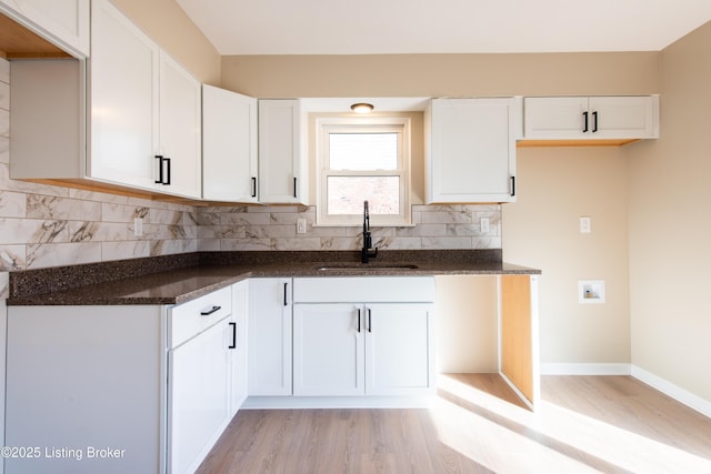 kitchen with dark stone counters, white cabinets, sink, tasteful backsplash, and light hardwood / wood-style floors