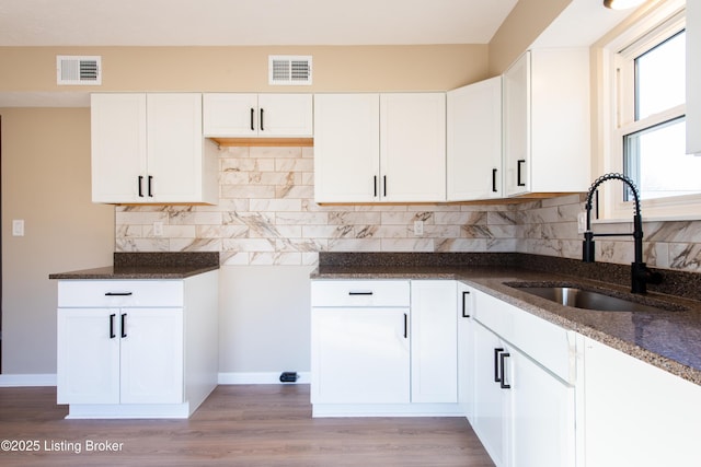 kitchen with tasteful backsplash, white cabinetry, dark stone counters, and sink