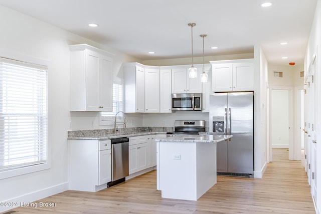 kitchen featuring a center island, white cabinets, hanging light fixtures, light stone counters, and stainless steel appliances