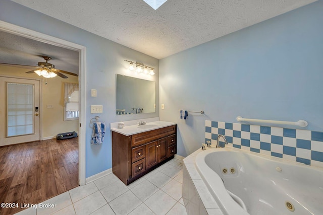 bathroom with ceiling fan, tile patterned floors, tiled tub, a textured ceiling, and vanity