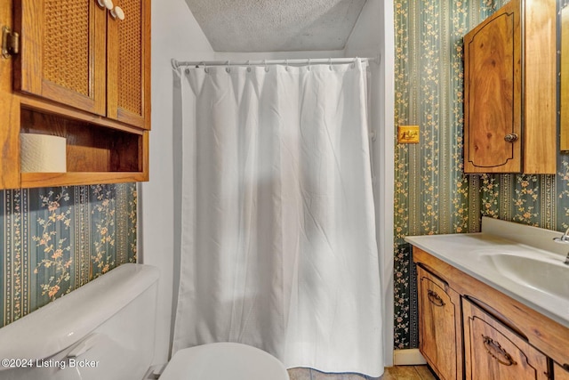 bathroom featuring vanity, a textured ceiling, toilet, and walk in shower