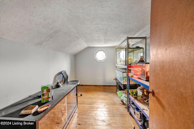 interior space featuring a textured ceiling, wood-type flooring, and vaulted ceiling