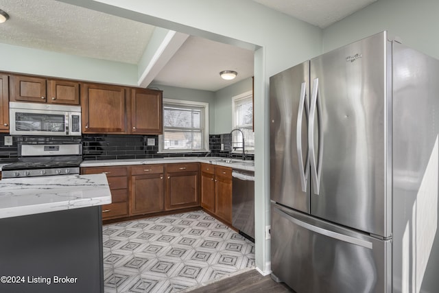 kitchen featuring light stone countertops, sink, a textured ceiling, decorative backsplash, and appliances with stainless steel finishes