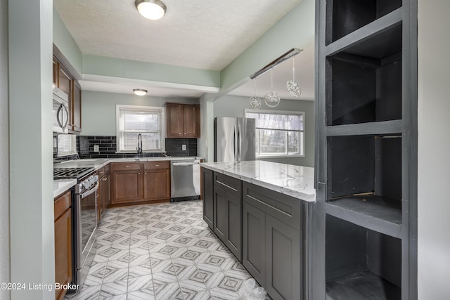 kitchen with decorative backsplash, light stone countertops, stainless steel appliances, sink, and decorative light fixtures