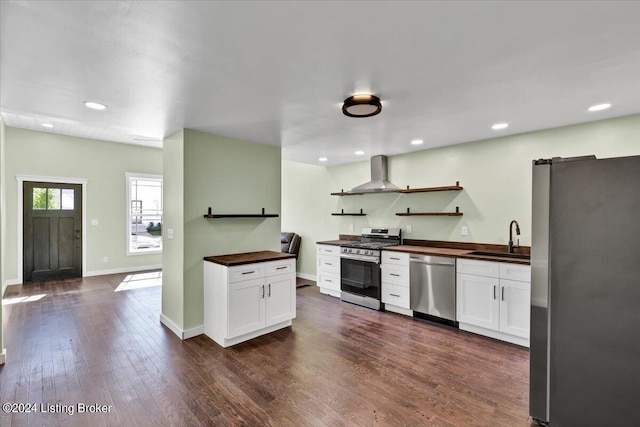 kitchen with appliances with stainless steel finishes, dark wood-type flooring, wall chimney range hood, sink, and white cabinets