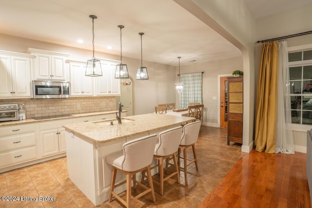 kitchen featuring sink, light stone countertops, black electric cooktop, an island with sink, and white cabinetry