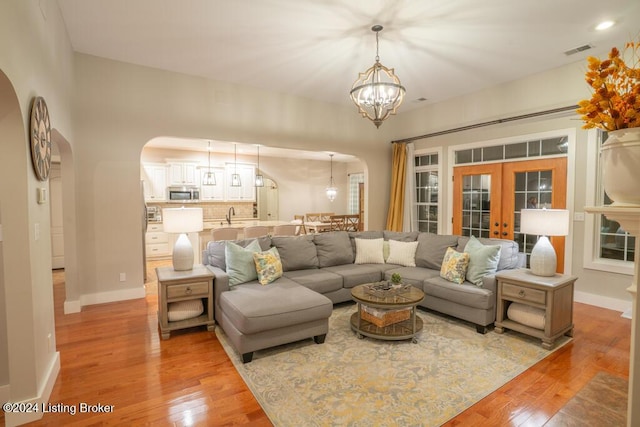 living room with a chandelier, light hardwood / wood-style floors, sink, and french doors