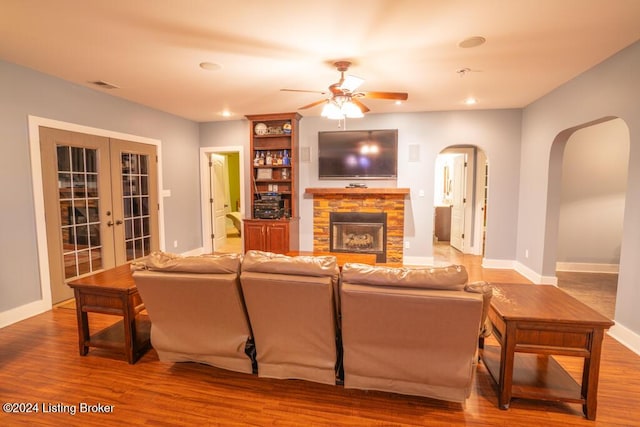 living room with french doors, a stone fireplace, ceiling fan, and hardwood / wood-style floors