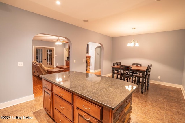 kitchen with pendant lighting, a center island, french doors, ceiling fan with notable chandelier, and dark stone countertops