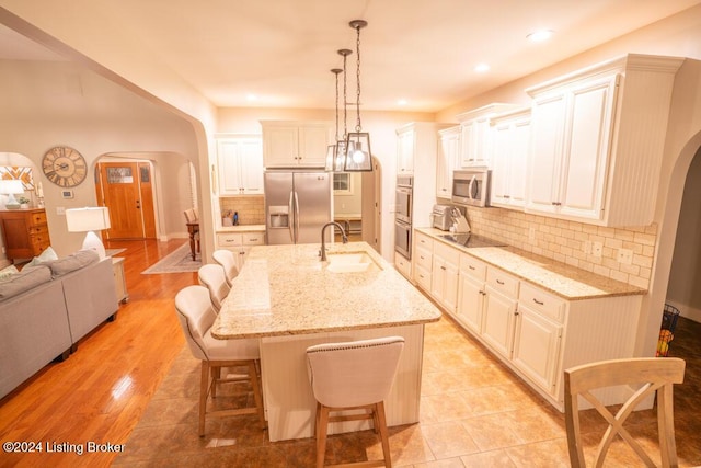 kitchen with appliances with stainless steel finishes, a breakfast bar, a kitchen island with sink, sink, and decorative light fixtures