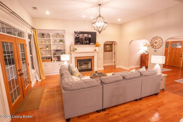 living room featuring a chandelier, built in features, light hardwood / wood-style flooring, and french doors