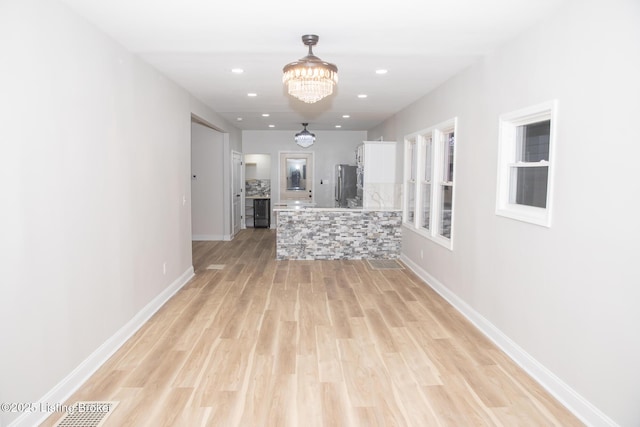 hall with light hardwood / wood-style floors and a notable chandelier