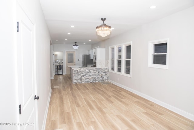 kitchen featuring light hardwood / wood-style flooring, hanging light fixtures, appliances with stainless steel finishes, kitchen peninsula, and white cabinets