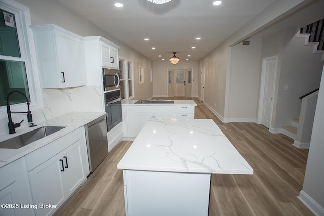 kitchen with sink, white cabinetry, a center island, light stone countertops, and black appliances