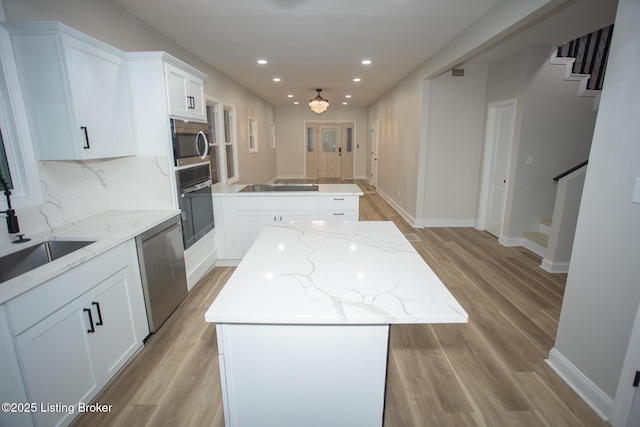 kitchen with light hardwood / wood-style flooring, a center island, light stone counters, black appliances, and white cabinets