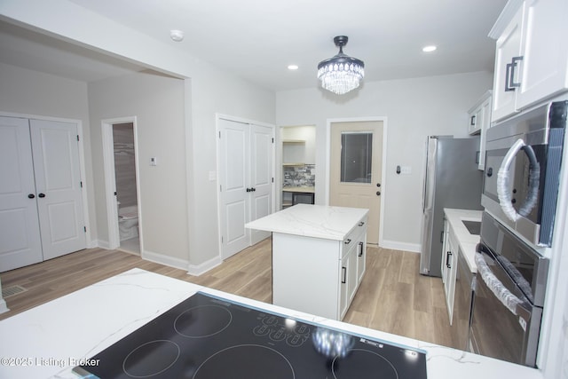 kitchen with white cabinetry, a center island, light stone counters, decorative light fixtures, and light wood-type flooring