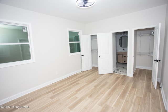 unfurnished bedroom with ensuite bath, light hardwood / wood-style floors, and a walk in closet