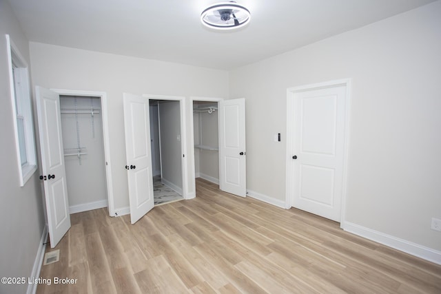 unfurnished bedroom featuring two closets and light hardwood / wood-style flooring