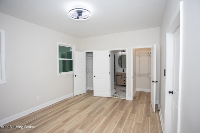 unfurnished bedroom with ensuite bath, a walk in closet, light hardwood / wood-style floors, and a closet