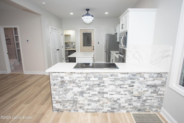 kitchen with appliances with stainless steel finishes, white cabinets, a notable chandelier, light hardwood / wood-style floors, and kitchen peninsula