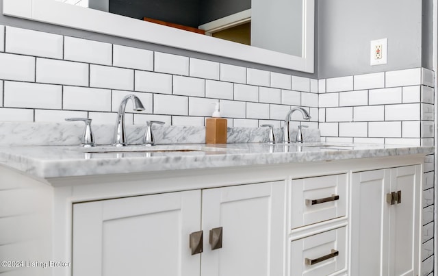 kitchen with sink, light stone counters, white cabinetry, and backsplash