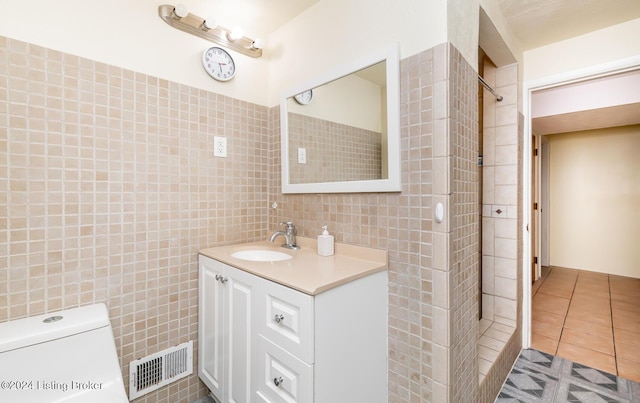 bathroom with a tile shower, tile patterned floors, toilet, vanity, and tile walls