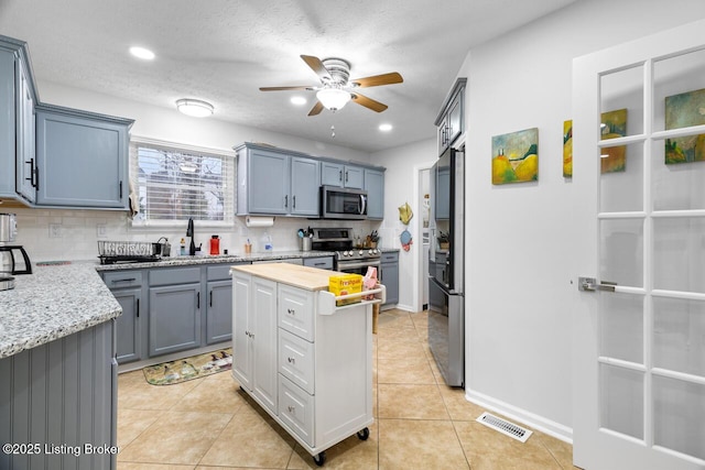 kitchen featuring appliances with stainless steel finishes, backsplash, a textured ceiling, ceiling fan, and light tile patterned floors