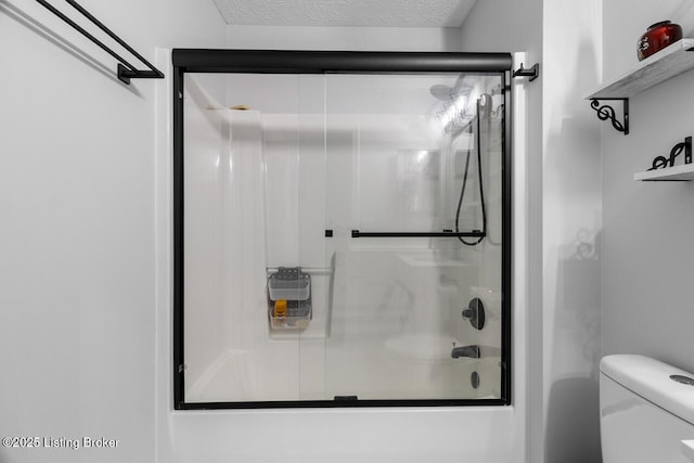 bathroom with toilet, combined bath / shower with glass door, and a textured ceiling