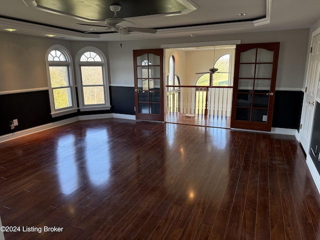 empty room with dark wood-type flooring, a tray ceiling, ceiling fan, and a healthy amount of sunlight