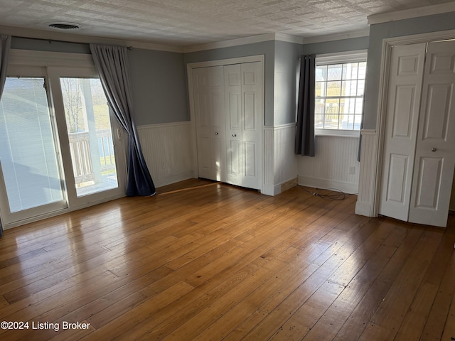 unfurnished bedroom with light wood-type flooring, crown molding, and multiple closets