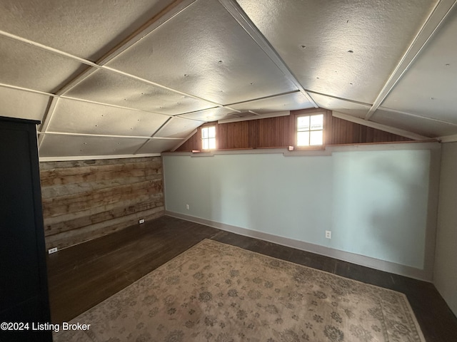 additional living space featuring wood walls, lofted ceiling, and a textured ceiling