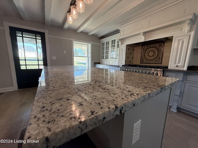 kitchen with a healthy amount of sunlight, light stone counters, beamed ceiling, hardwood / wood-style floors, and white cabinets