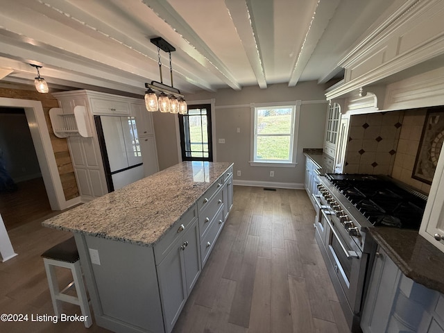 kitchen featuring range with two ovens, hanging light fixtures, fridge, beamed ceiling, and a kitchen island