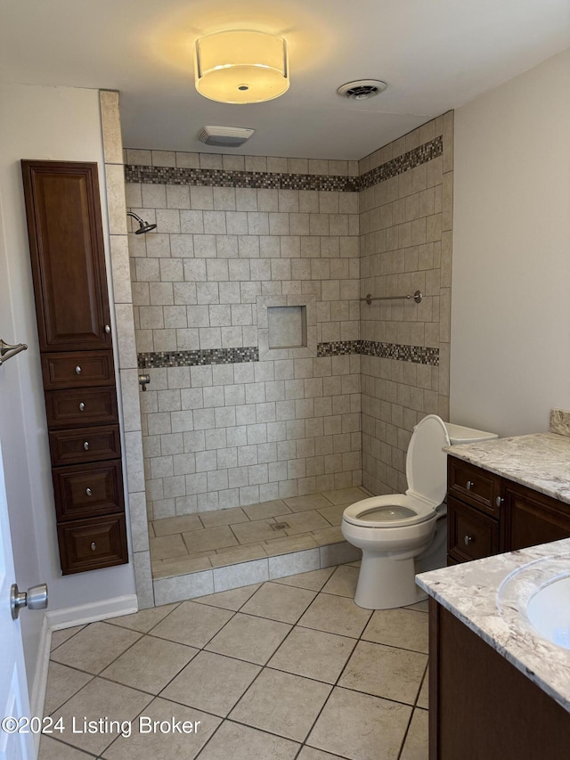 bathroom with toilet, tile patterned flooring, vanity, and tiled shower